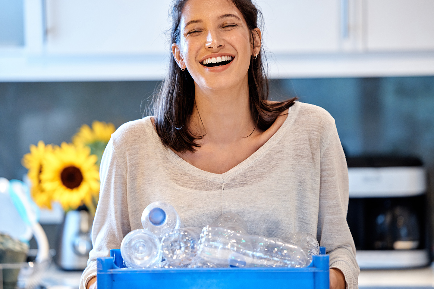 A person holds a blue box full of recycling.